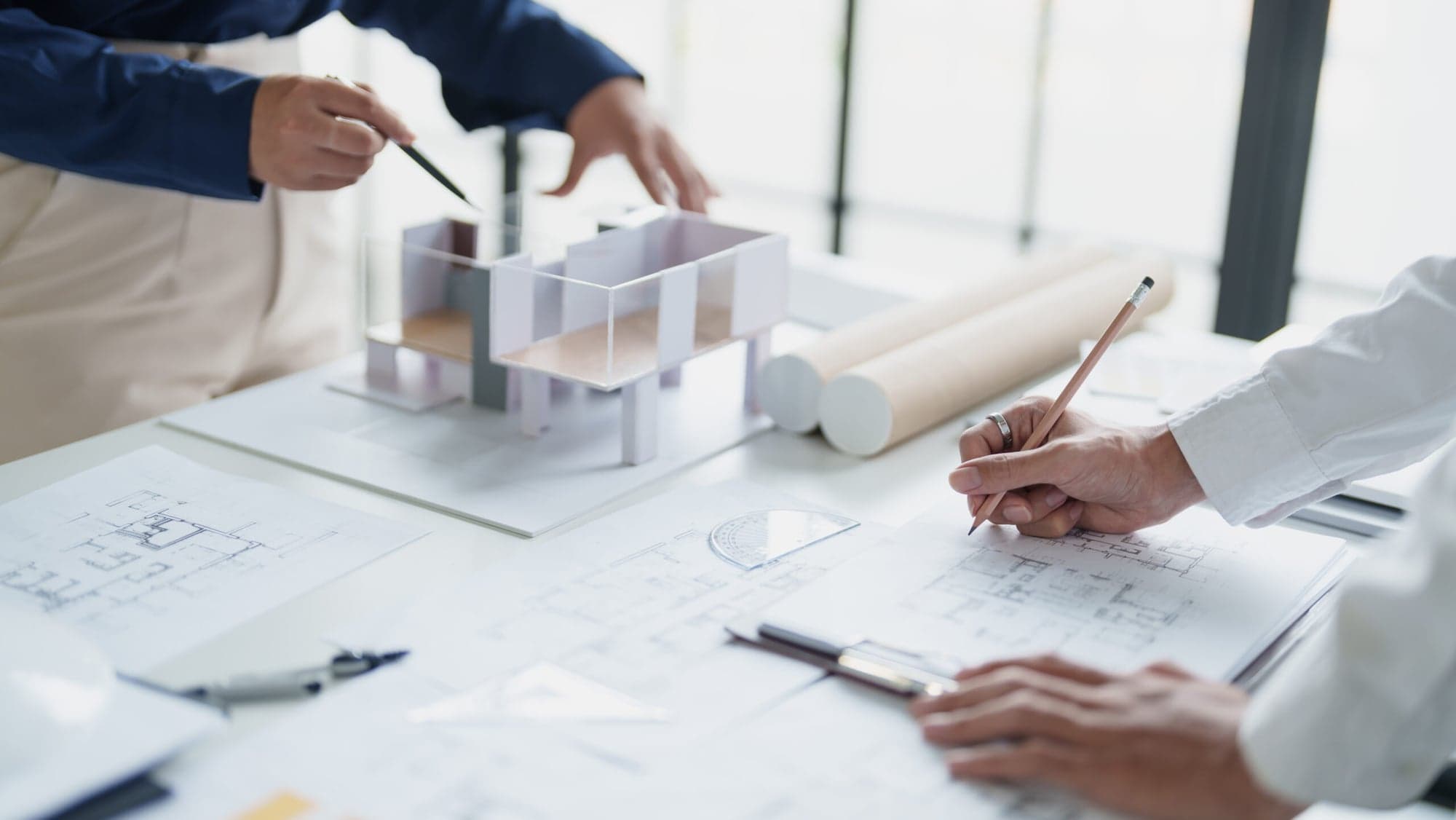 Architect working on an architectural model with a pen and plans, concept and design by fbnSTUDIO